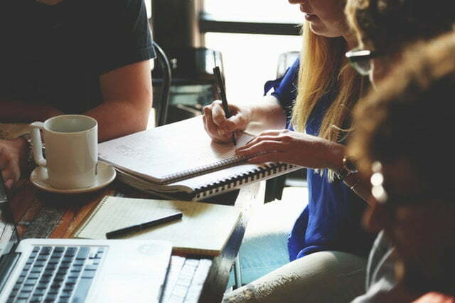 a group of people sitting at a table with a laptop and a coffee cup