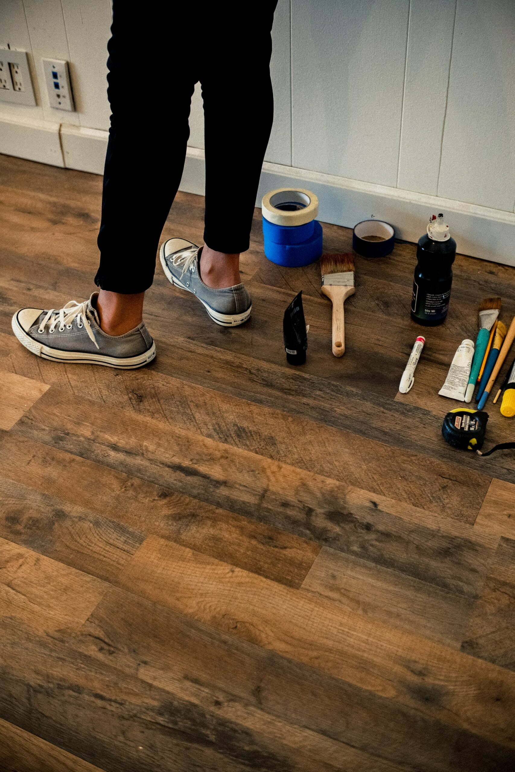 a person standing on a wood floor with tools and a can