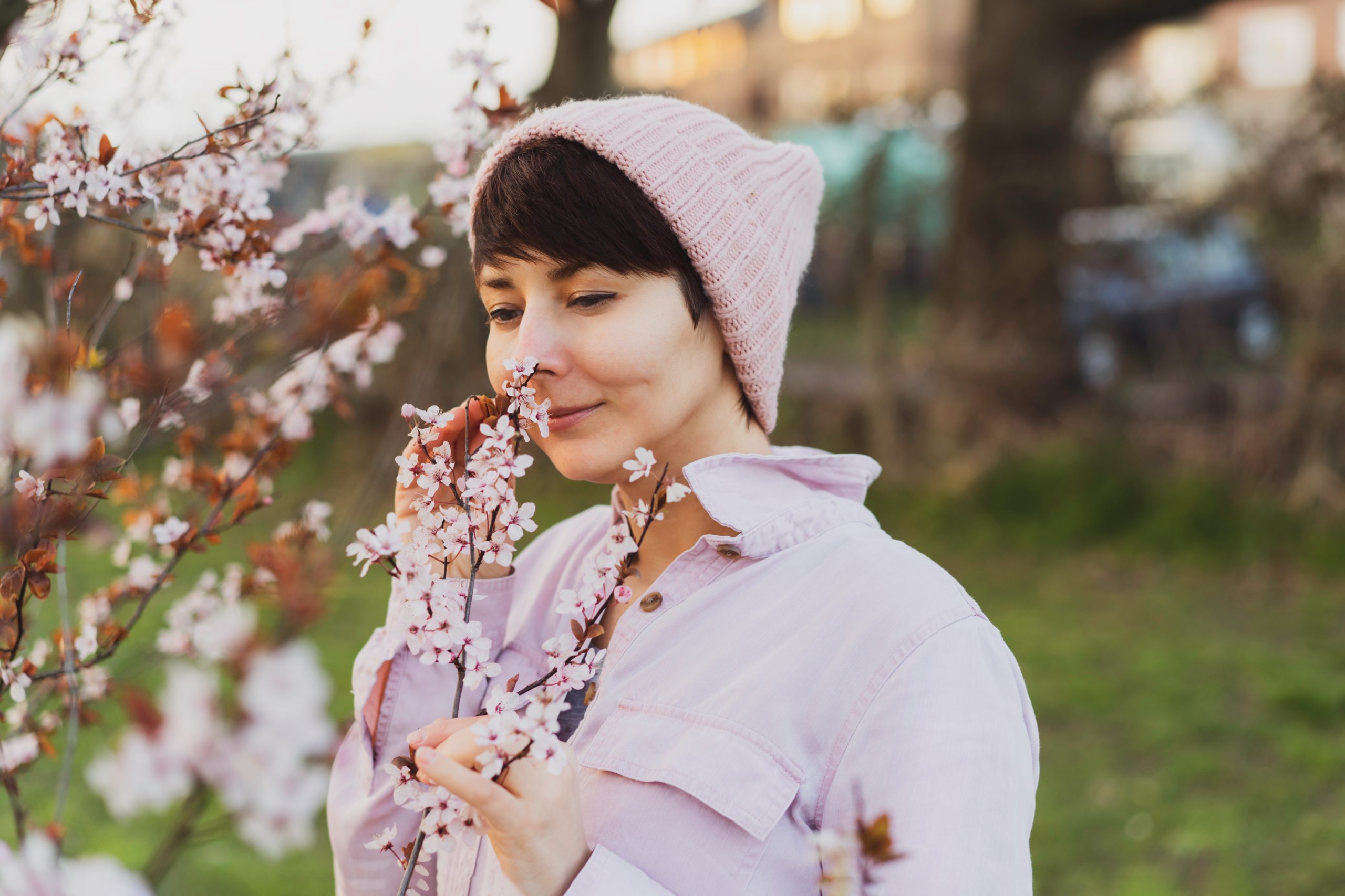 Woman in pink clothes sniffing blooming branches with pink flowers. Enjoying springtime